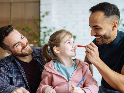 Mid adult gay couple at home with daughter, drawing and playing together. Getty Images. Credit: Drazen_