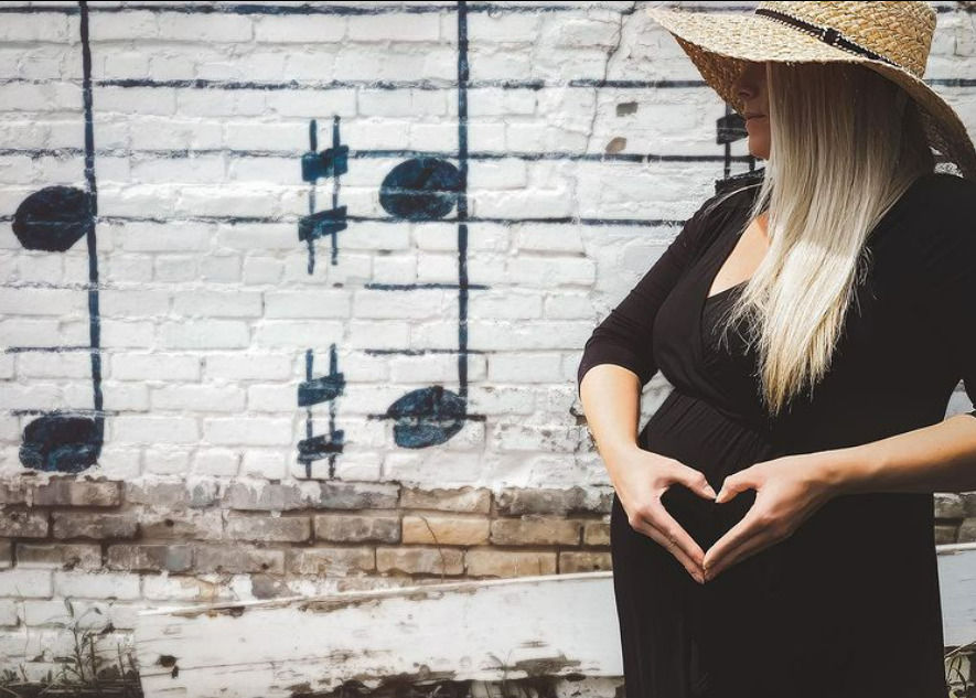 pregnant woman with hands in shape of heart posing in front of music note wall mural