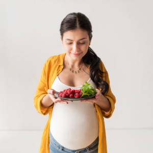 Pregnant woman holds a plate of fruit.