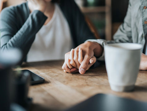 Close-up of a couple holding hands at a table, offering emotional support to one another, symbolizing hope and healing after a nonviable pregnancy through the option of surrogacy.