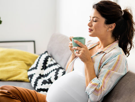 Pregnant woman resting on sofa drinking coffee. Source: Getty Images. Credit: Nastasic.