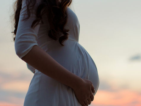 Pregnant woman in a white dress standing outdoors with the sky in the background (model)