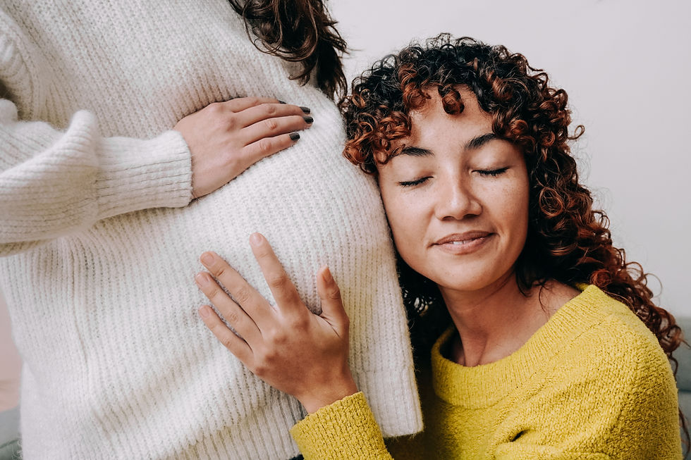 Model closes her eyes and rests the side of her face against a pregnant woman's belly and rests her hand on the baby bump.