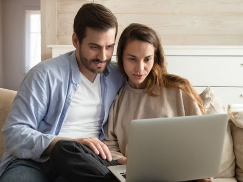 Couple sitting on a couch looking at a laptop together (models)