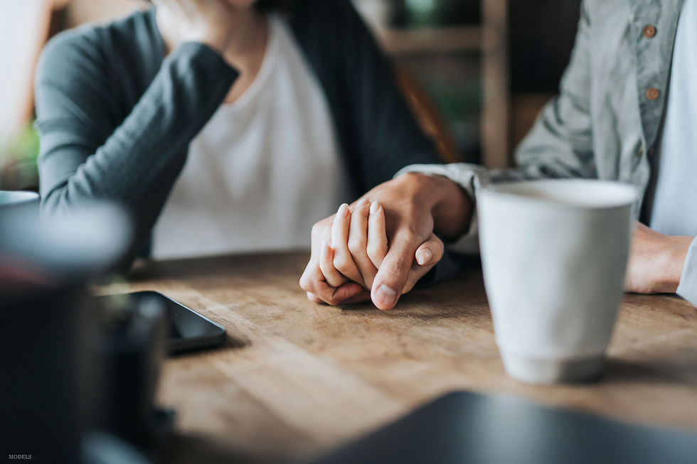 Closeup of a couple holding hands while a medical professional sits next to them while writing on a clipboard.