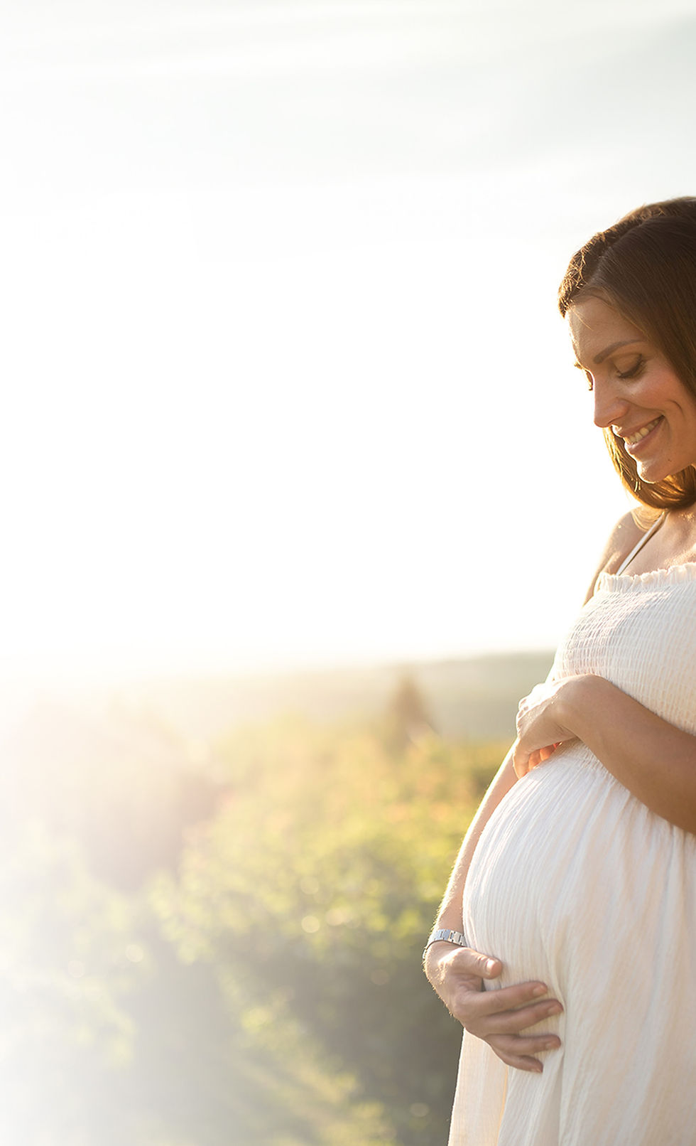 Smiling pregnant woman in white dress, glowing sunset